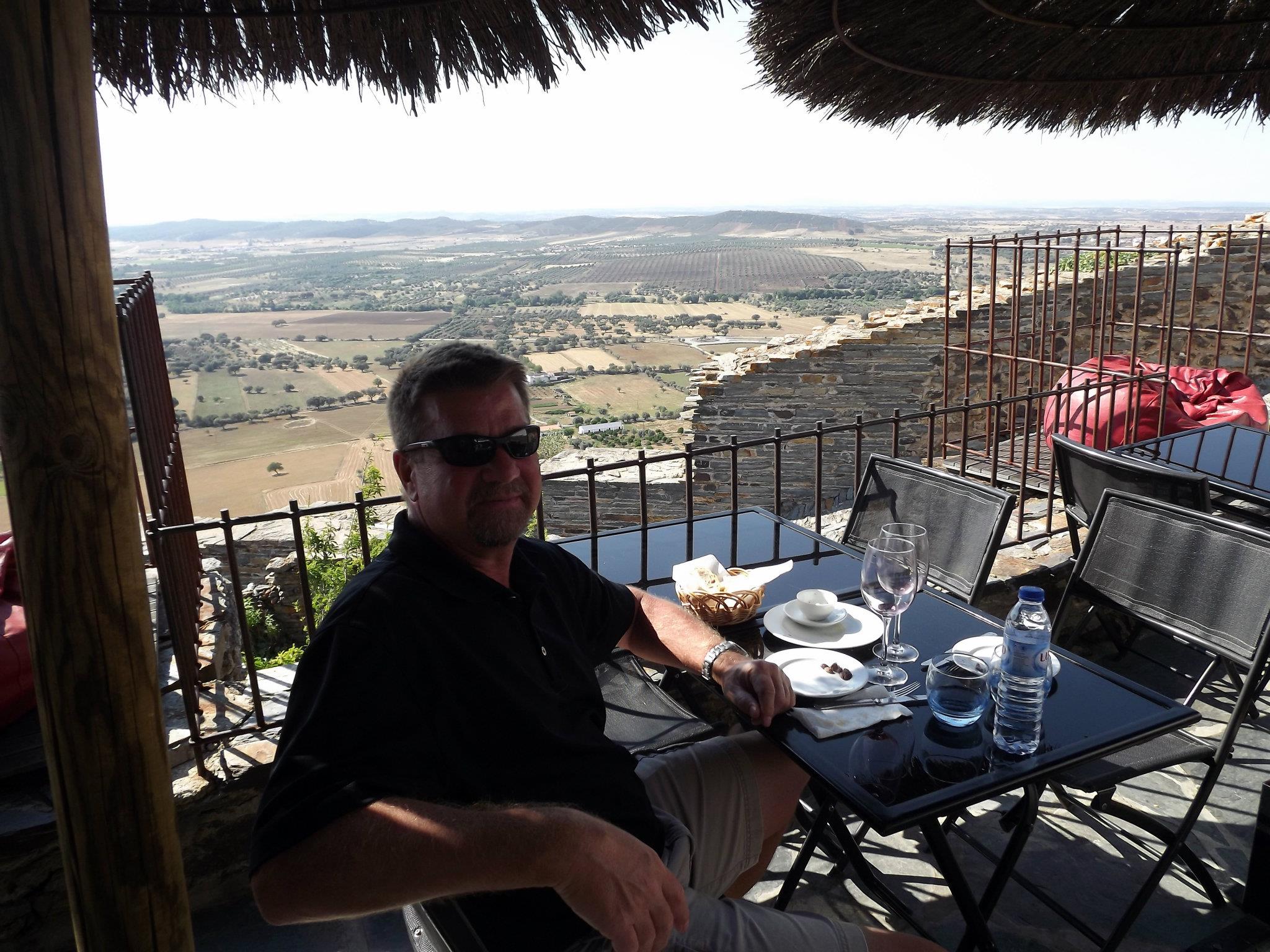 man at a restaurant table drinking water overlooking countryside
