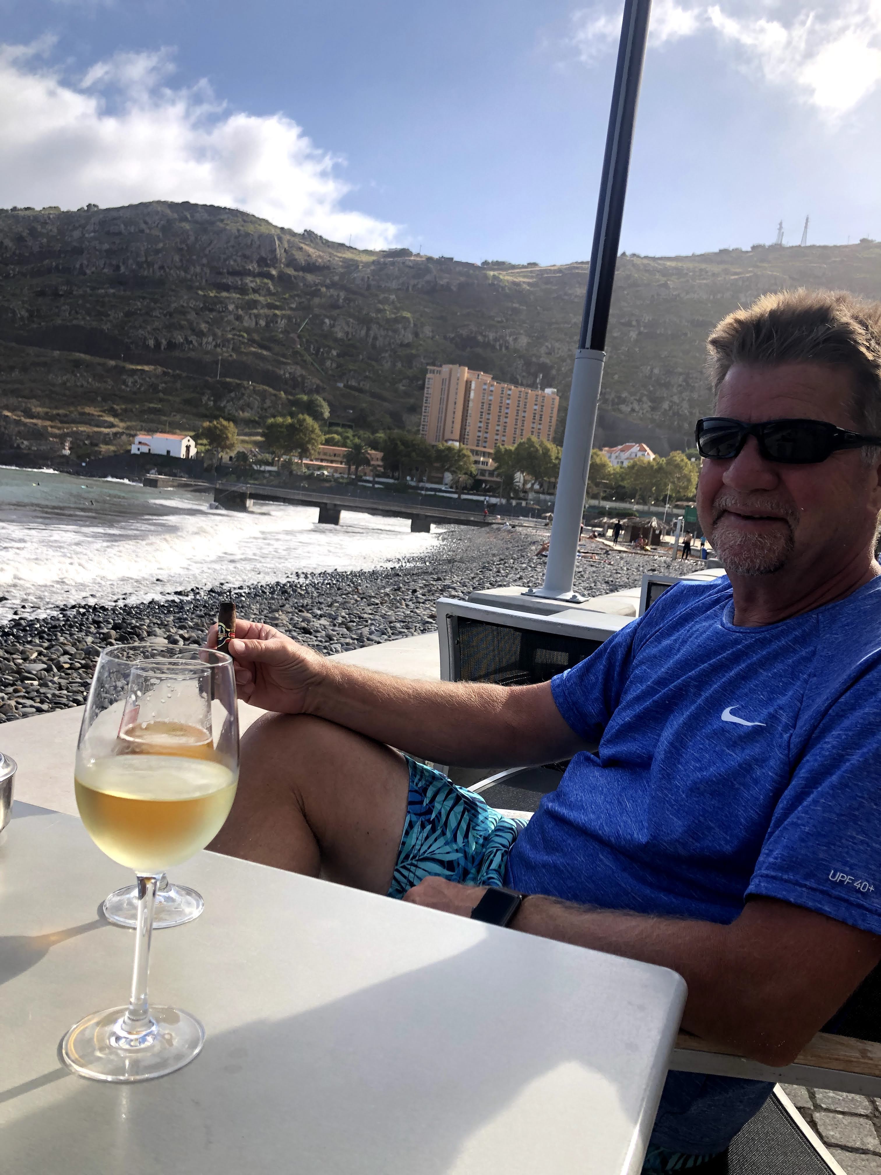 man having wine and smoking cigar by the rocky beach